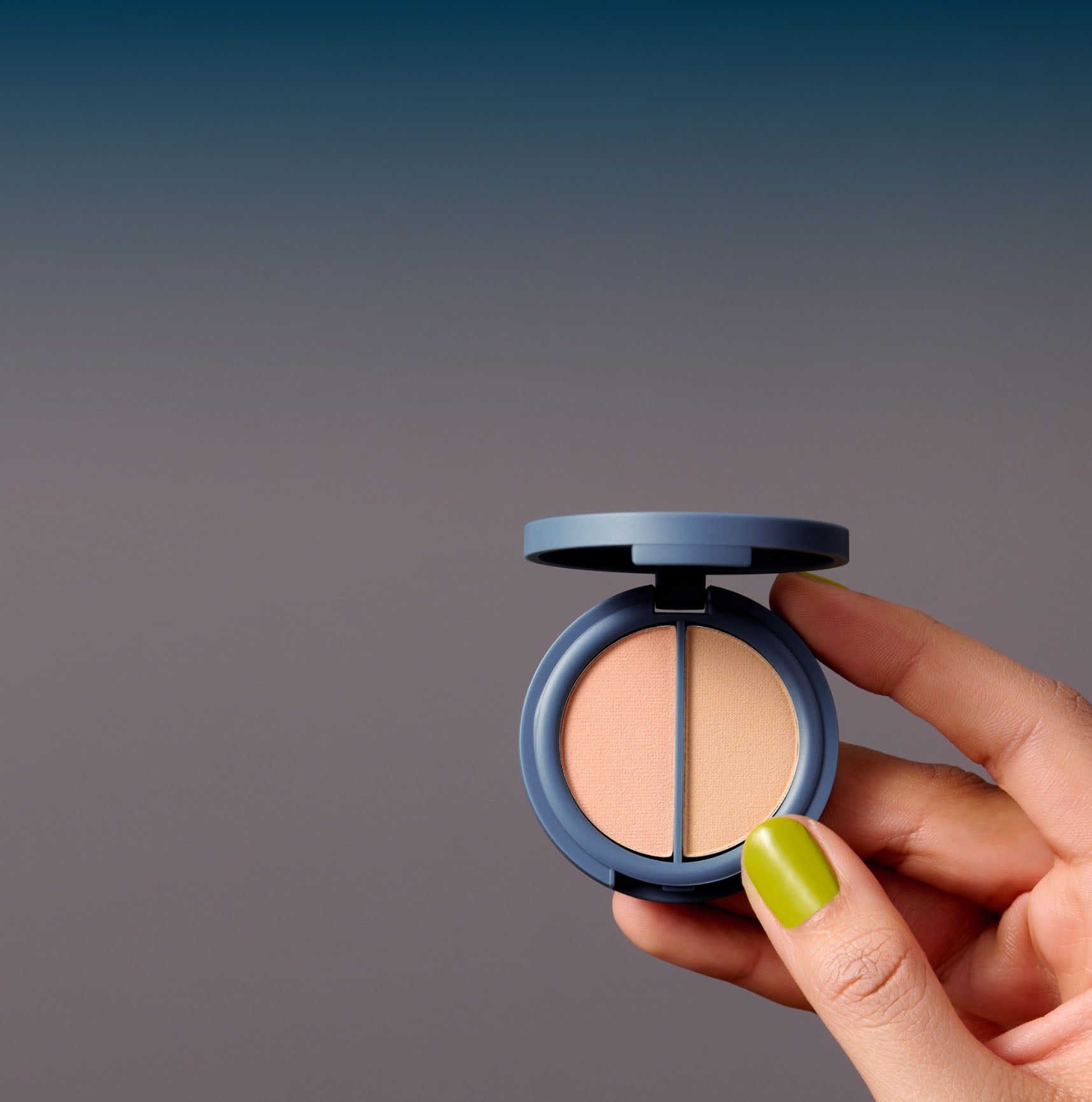 A hand holds a teal colored powder makeup compact with two peach colored half-circle pans of powder inside