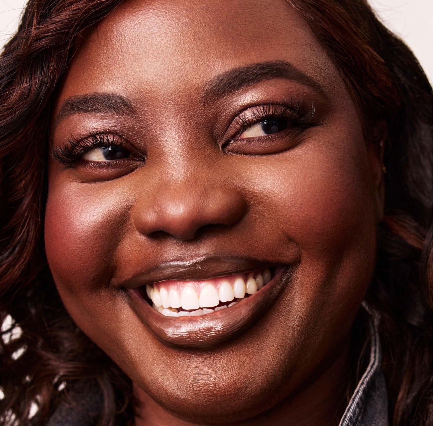 A smiling woman with a denim jacket looks to the side on a white background