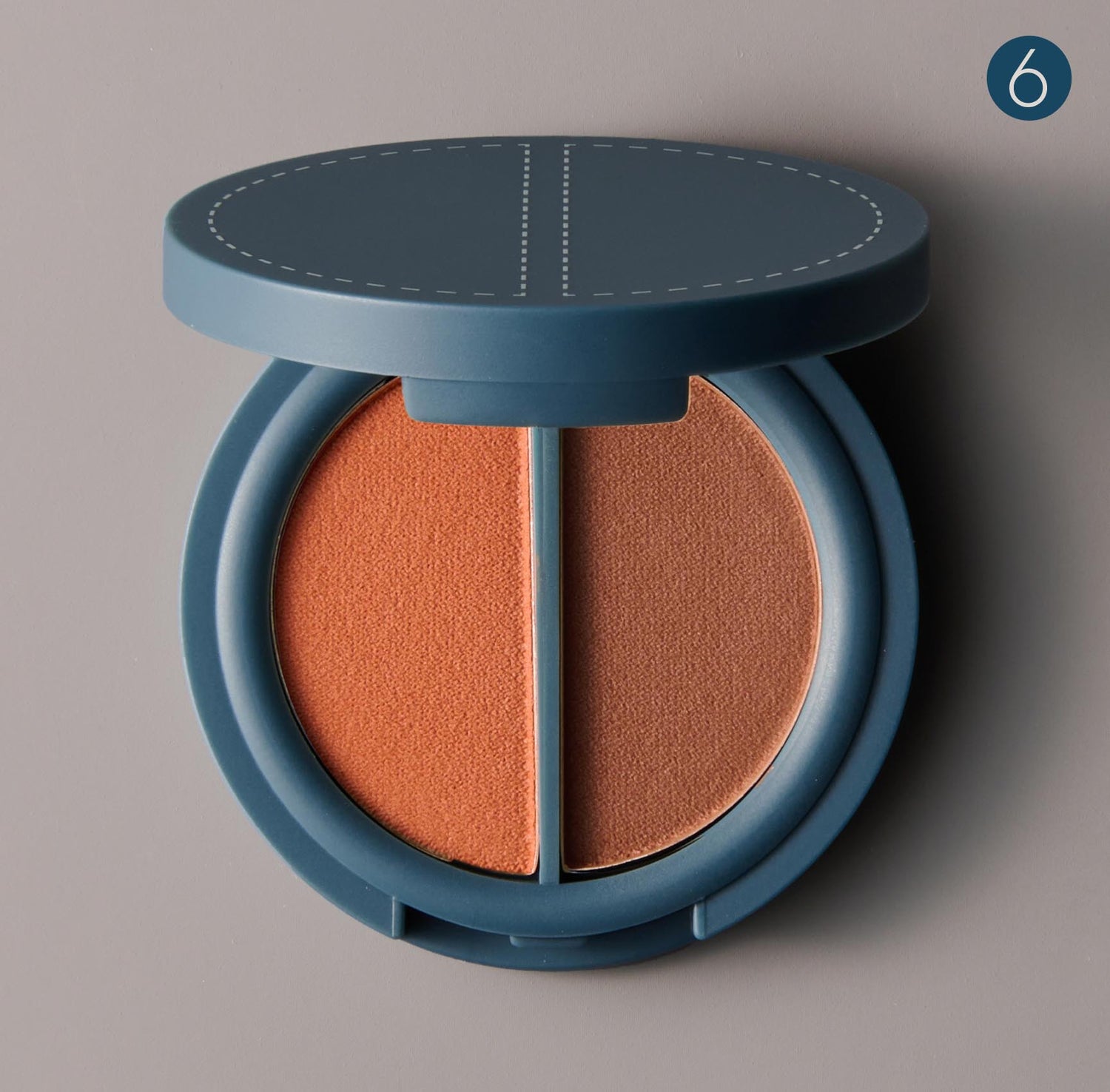 a round teal colored makeup compact with two shades of warm brown pressed powder on a gray background and the number 6 labeling the upper righthand corner